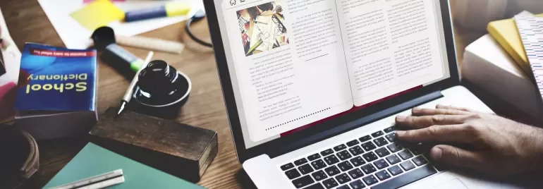 Manos escribiendo en un portátil, rodeado de libros y herramientas de estudio.