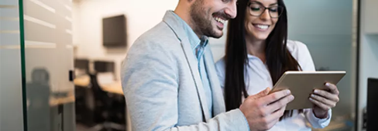 Pareja de profesionales sonriendo mientras revisan una tableta en la oficina.