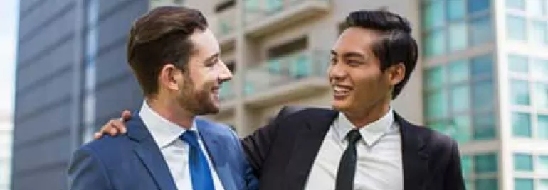 Dos hombres de negocios sonrientes, vestidos con traje y corbata, hablando afuera de un edificio moderno.