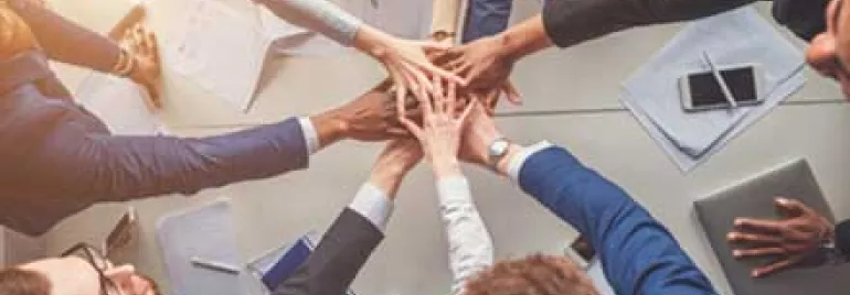 Personas uniendo manos en un gesto de trabajo en equipo.