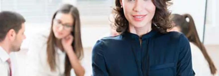 Mujer sonriendo con equipo trabajando detrás.