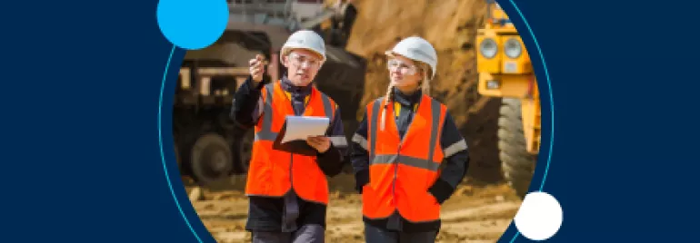 Dos ingenieros con chalecos naranjas discuten en un sitio de construcción.