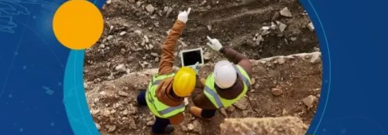 Dos trabajadores de la construcción revisan una tablet en un sitio de excavación.