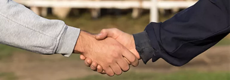 Dos personas estrechándose la mano en un entorno rural.
