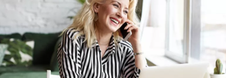 Mujer sonriendo hablando por teléfono junto a computadora.