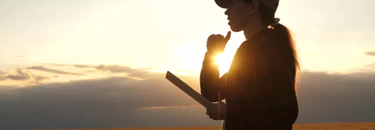 Persona en un campo con una tableta al atardecer.
