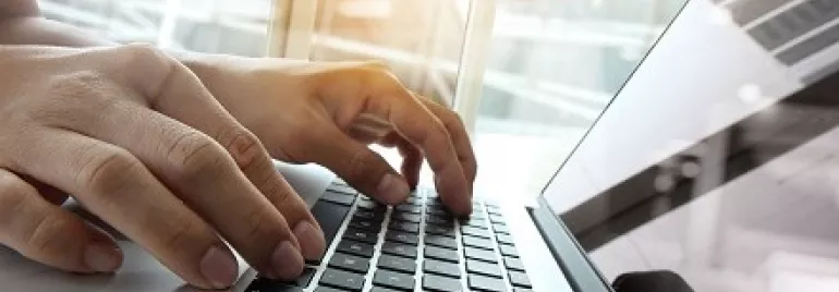 Manos escribiendo en un teclado de computadora iluminada por la luz.