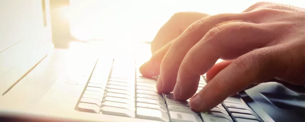 Manos escribiendo en un teclado de computadora blanca iluminada.