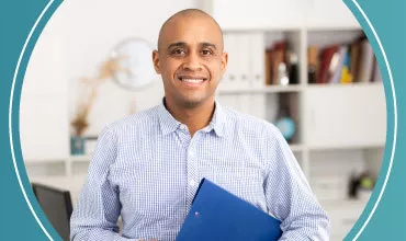 Hombre sonriente con camisa a cuadros sosteniendo carpeta azul en oficina.