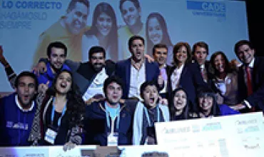 Grupo de jóvenes en evento de CADE Universitario sonríen juntos en escenario.