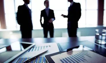 Personas discutiendo en una oficina con gráficos en primer plano.
