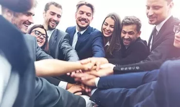 Grupo de personas en traje uniendo manos en un gesto de trabajo en equipo.