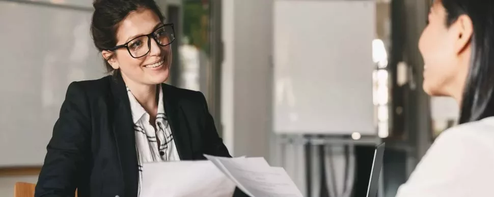 Mujer con gafas sonriendo mientras sostiene documentos en una reunión.