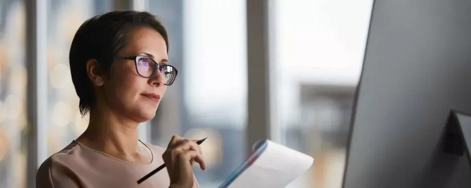 Mujer con gafas mirando el monitor mientras toma notas.