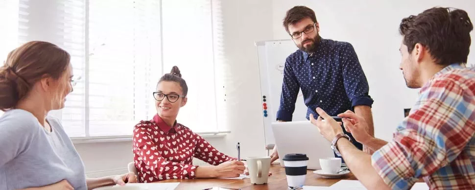 Grupo de personas en reunión alrededor de una mesa con portátil y café.