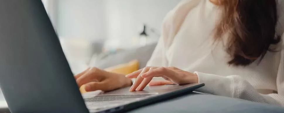 Mujer en suéter blanco usando computadora portátil en sofá.