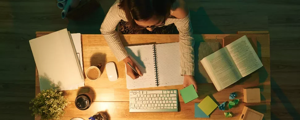 Persona trabajando en un escritorio con libreta abierta y varios papeles de colores.