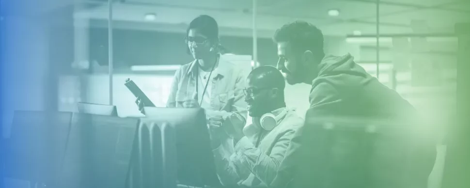 Tres personas trabajando juntas en una oficina con computadoras.