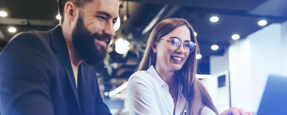 Dos personas sonrientes mirando una pantalla en una oficina moderna.
