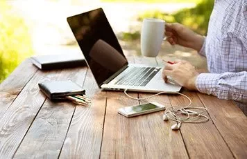 Persona trabajando al aire libre con laptop y taza de café.