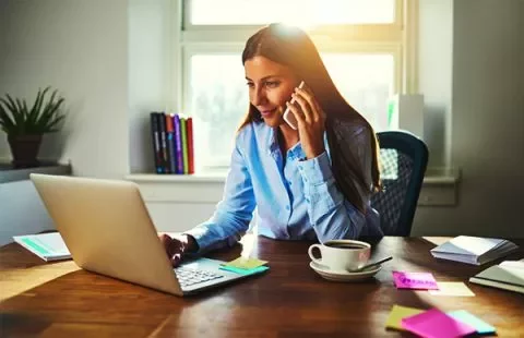 Mujer trabajando en una laptop y hablando por teléfono.