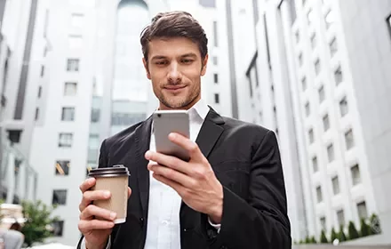 Hombre en traje sonríe mientras mira su teléfono en la calle.