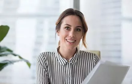 Mujer sonriendo con camisa de rayas, sosteniendo papeles.