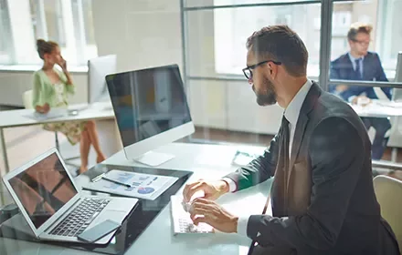 Hombre con gafas trabajando en una oficina moderna con computadora y gráficos.