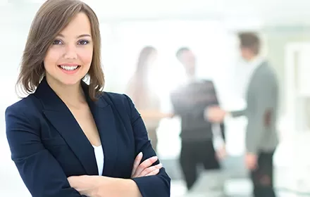 Mujer sonriente en primer plano con colegas difuminados al fondo.