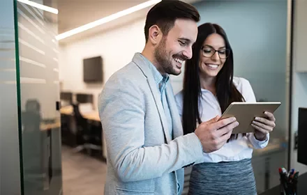 Pareja de profesionales sonriendo mientras revisan una tableta en la oficina.