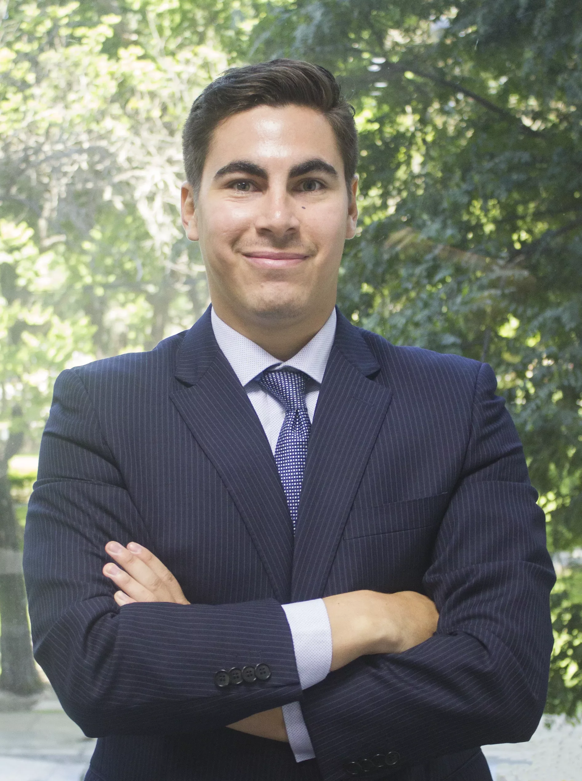 Hombre sonriente con traje y corbata delante de árboles.