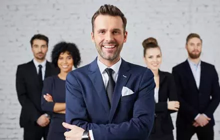 Hombre de negocios sonriente en el centro con colegas al fondo.