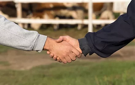 Dos personas estrechándose la mano en un entorno rural.