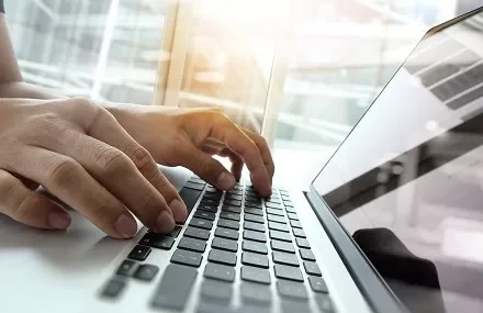 Manos escribiendo en un teclado de computadora iluminada por la luz.